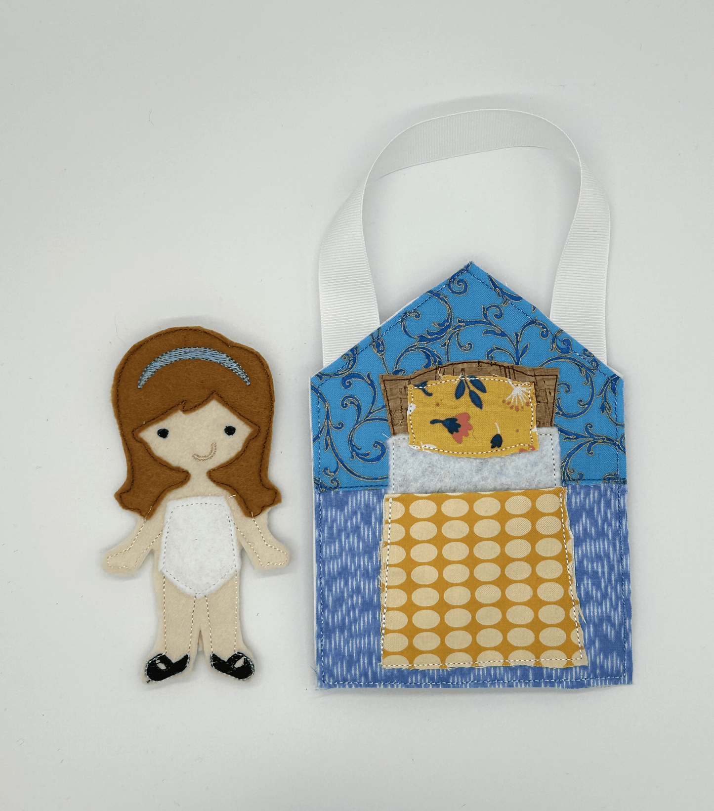 Felt and cloth "paper style" doll beside cloth bed and blanket